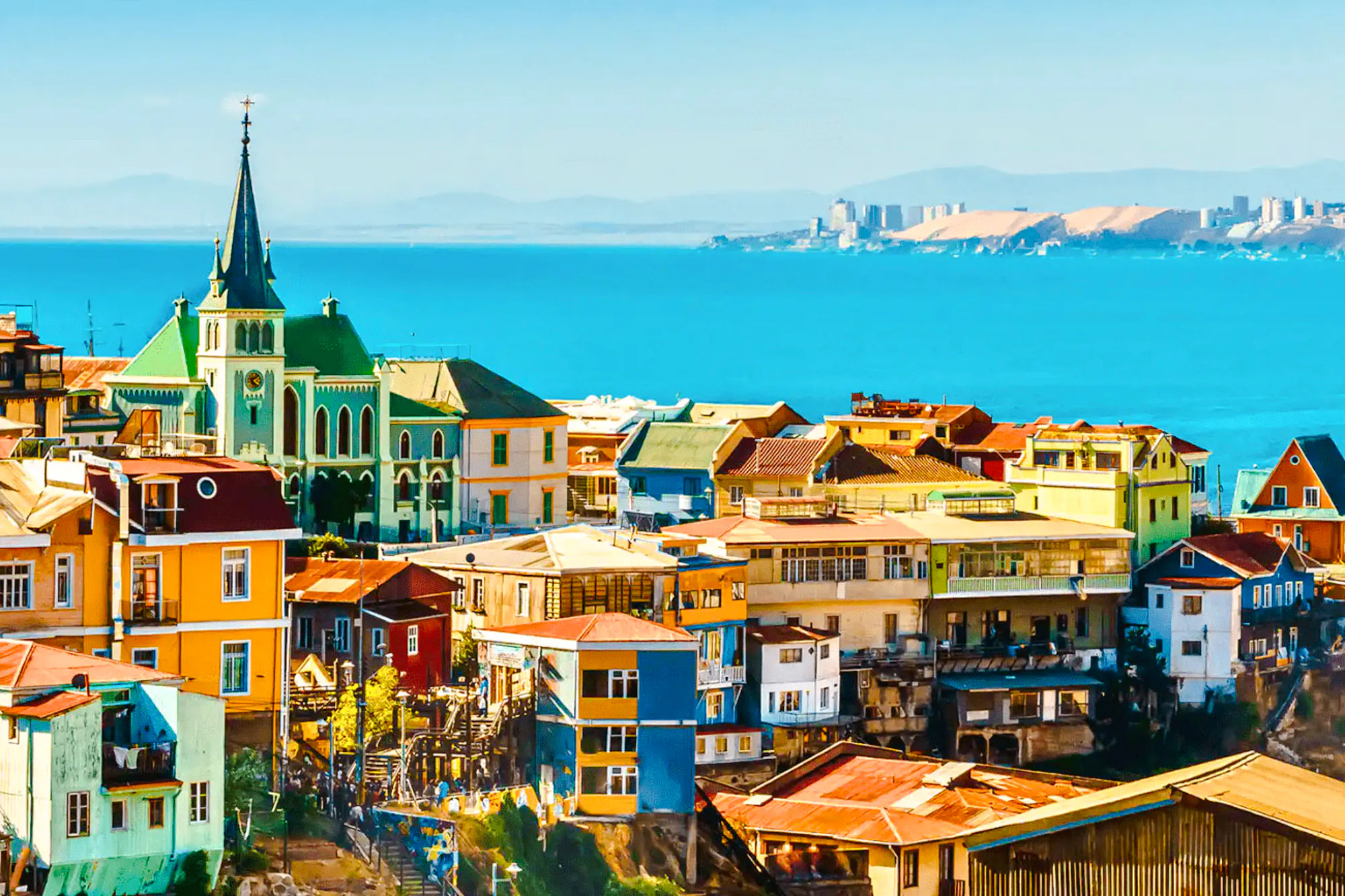 Colorful hillside houses and a church in Valparaíso, Chile, overlooking the Pacific Ocean.