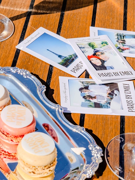 Champagne and macarons on a table with Paris-themed photos, Emily in Paris Seine Cruise.