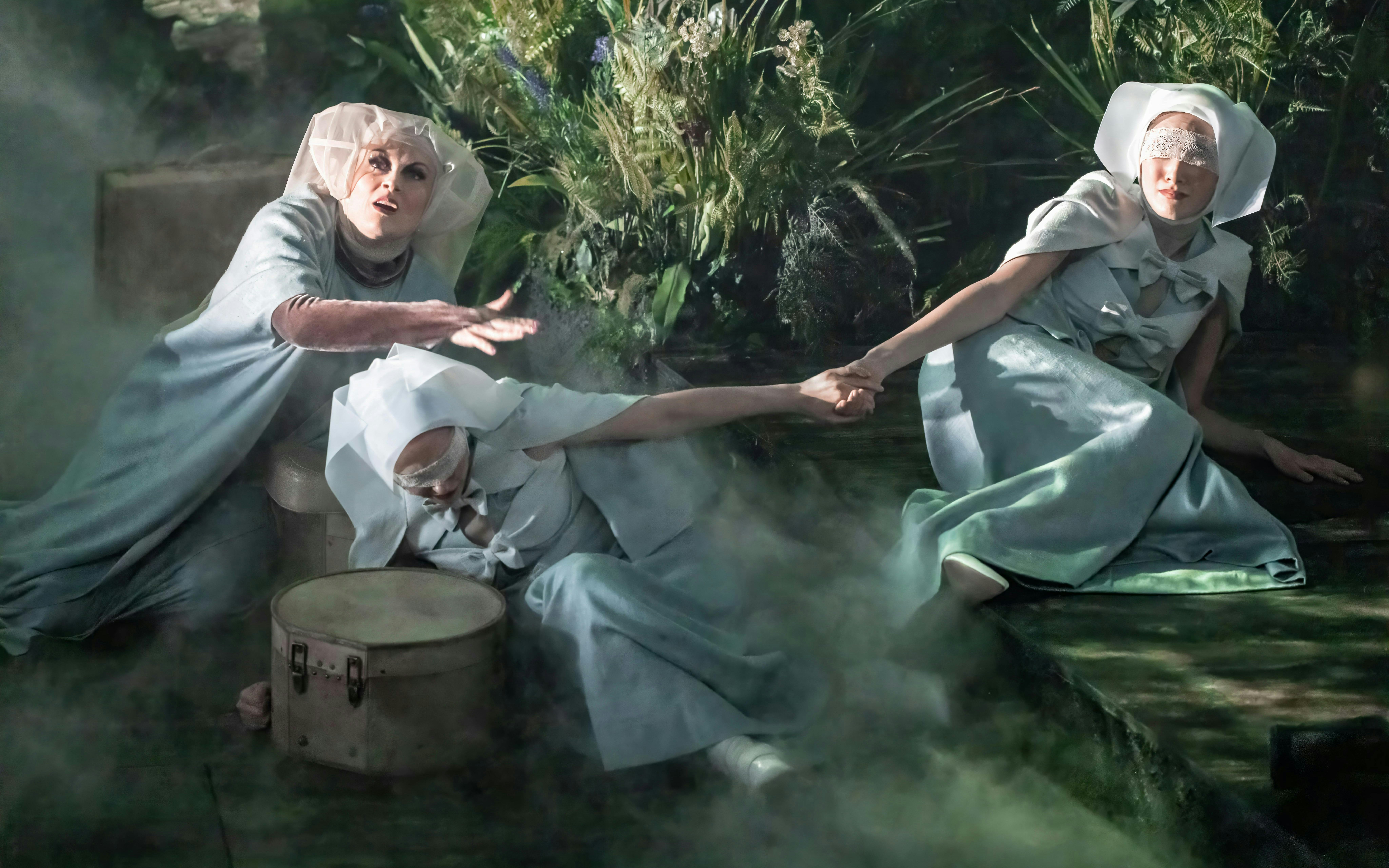 Actors in ethereal costumes perform a scene from "Into The Woods" amidst a misty forest setting.