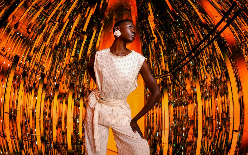 Person standing in a reflective, orange-lit room at AYA Universe.