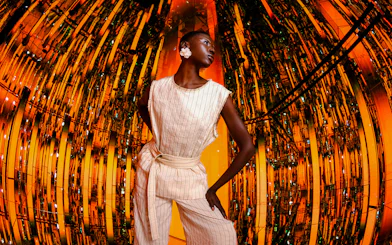 Person standing in a reflective, orange-lit room at AYA Universe.