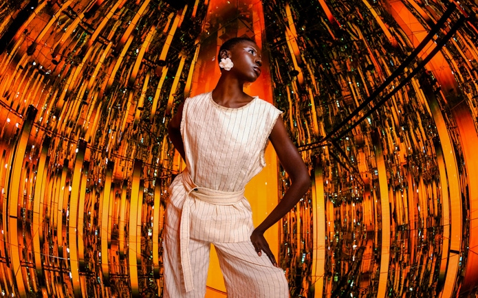 Person standing in a reflective, orange-lit room at AYA Universe.