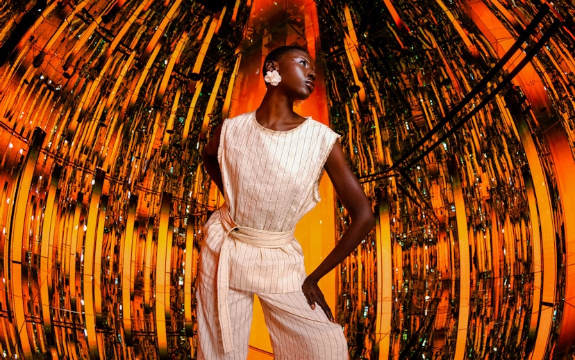 Person standing in a reflective, orange-lit room at AYA Universe.