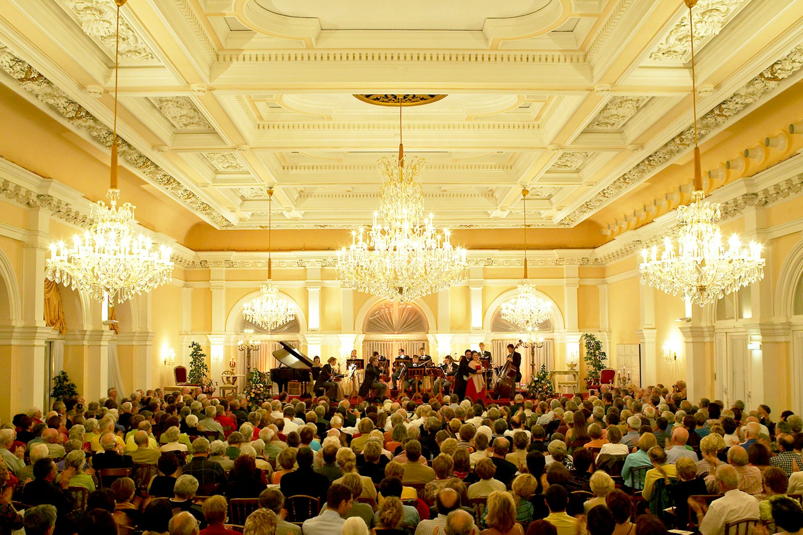Orchestra performing at Kursalon Vienna with audience seated under chandeliers.