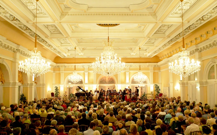 Orchestra performing at Kursalon Vienna with audience seated under chandeliers.