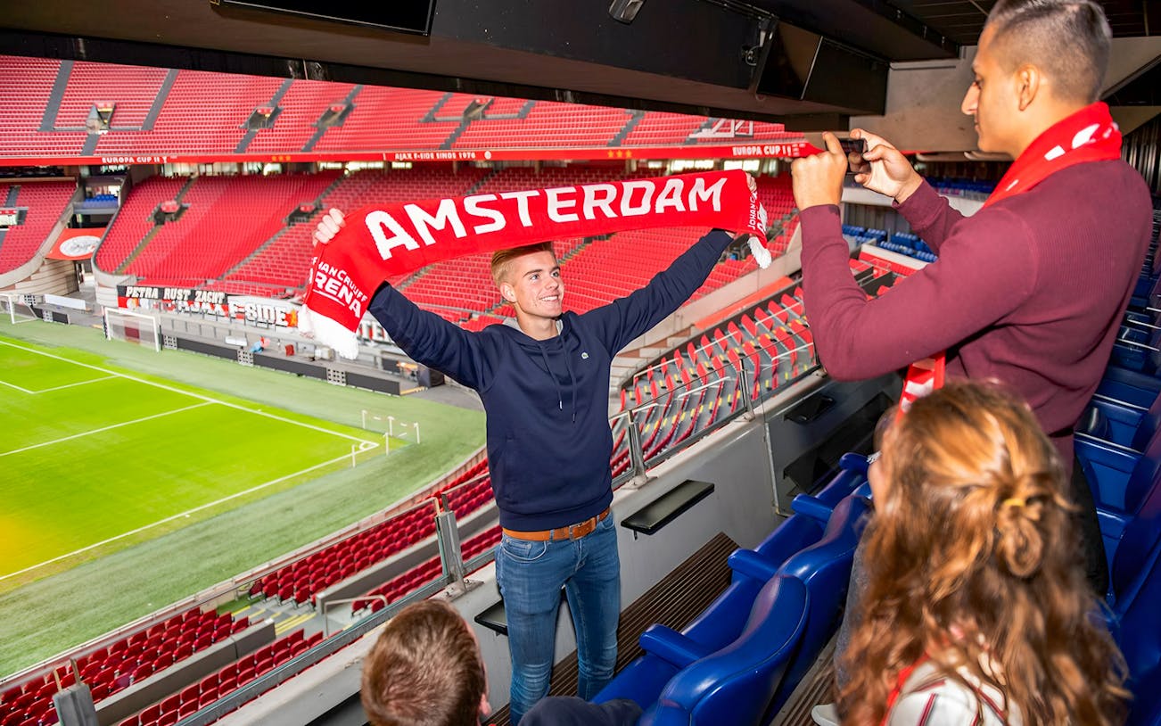 Man holding Amsterdam scarf at Johan Cruijff ArenA during VIP tour.