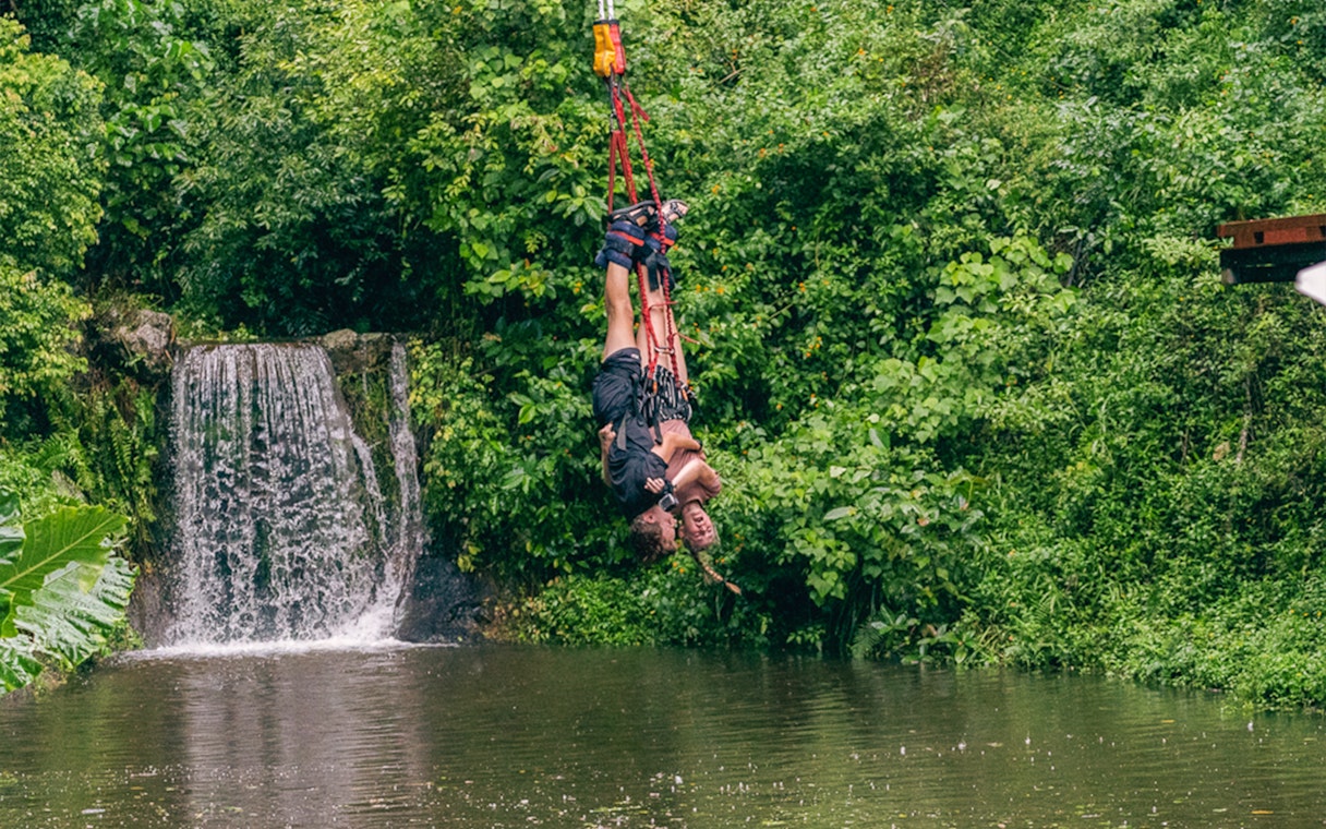 Bungy jumper over lush greenery and waterfall in Cairns, Australia.