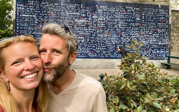 Couple in front of the I Love You Wall in Montmartre, Paris during a romantic walking tour.
