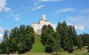 Trakošćan Castle in Croatia surrounded by lush green trees under a clear blue sky.