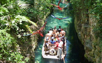 Tourists on a boat ride through a lush canal with macaws flying overhead at Xcaret Park.
