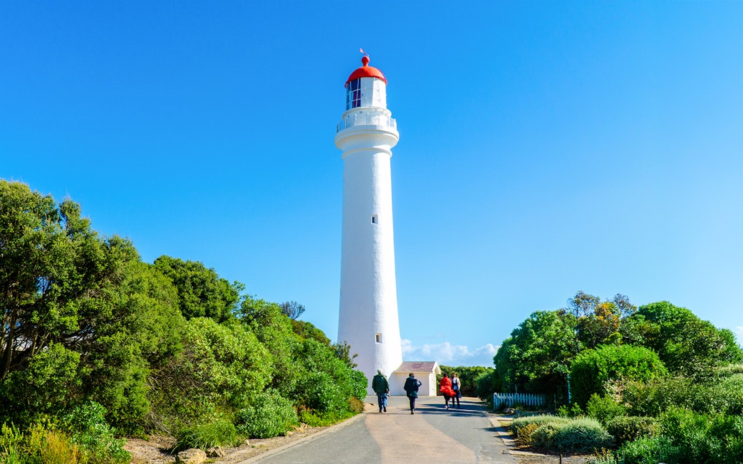 People walking on a path towards Split Point Lighthouse surrounded by greenery.