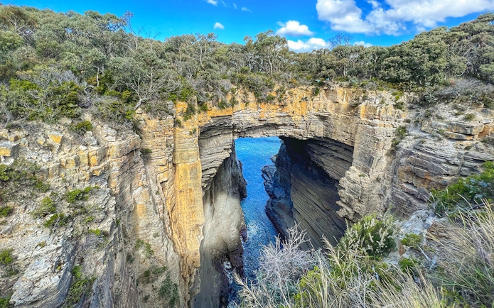 Natural rock arch formation at Port Arthur, Tasmania, with blue ocean visible through the opening.