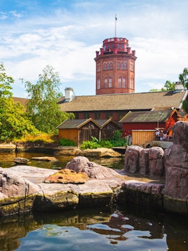 Skansen Museum tower with surrounding traditional wooden buildings and rocky water feature.