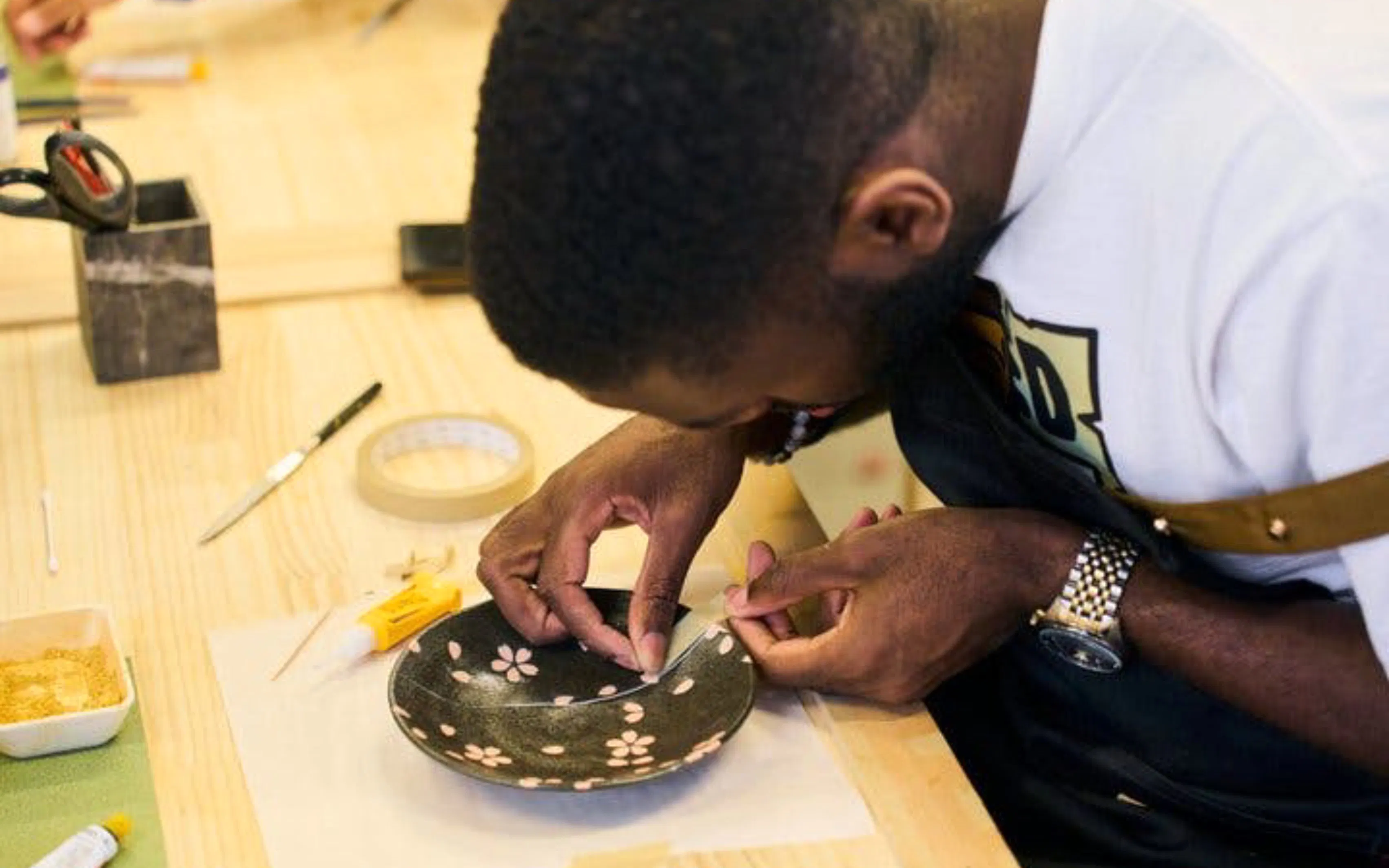 Person repairing a ceramic bowl using kintsugi technique in a Tokyo workshop.