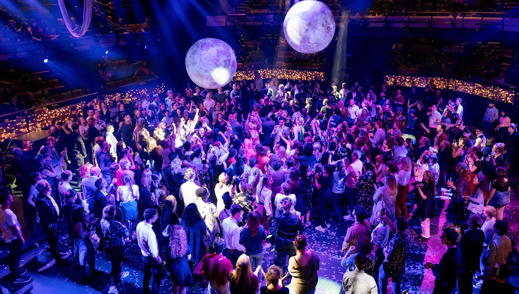 Crowd enjoying A Midsummer Night's Dream performance at a seated venue with vibrant lighting.