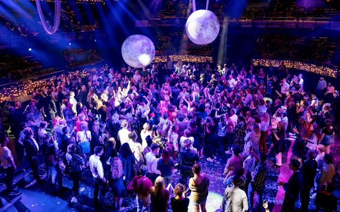 Crowd enjoying A Midsummer Night's Dream performance at a seated venue with vibrant lighting.