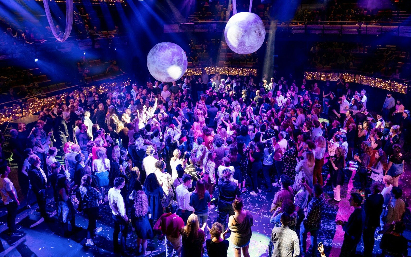 Crowd enjoying A Midsummer Night's Dream performance at a seated venue with vibrant lighting.