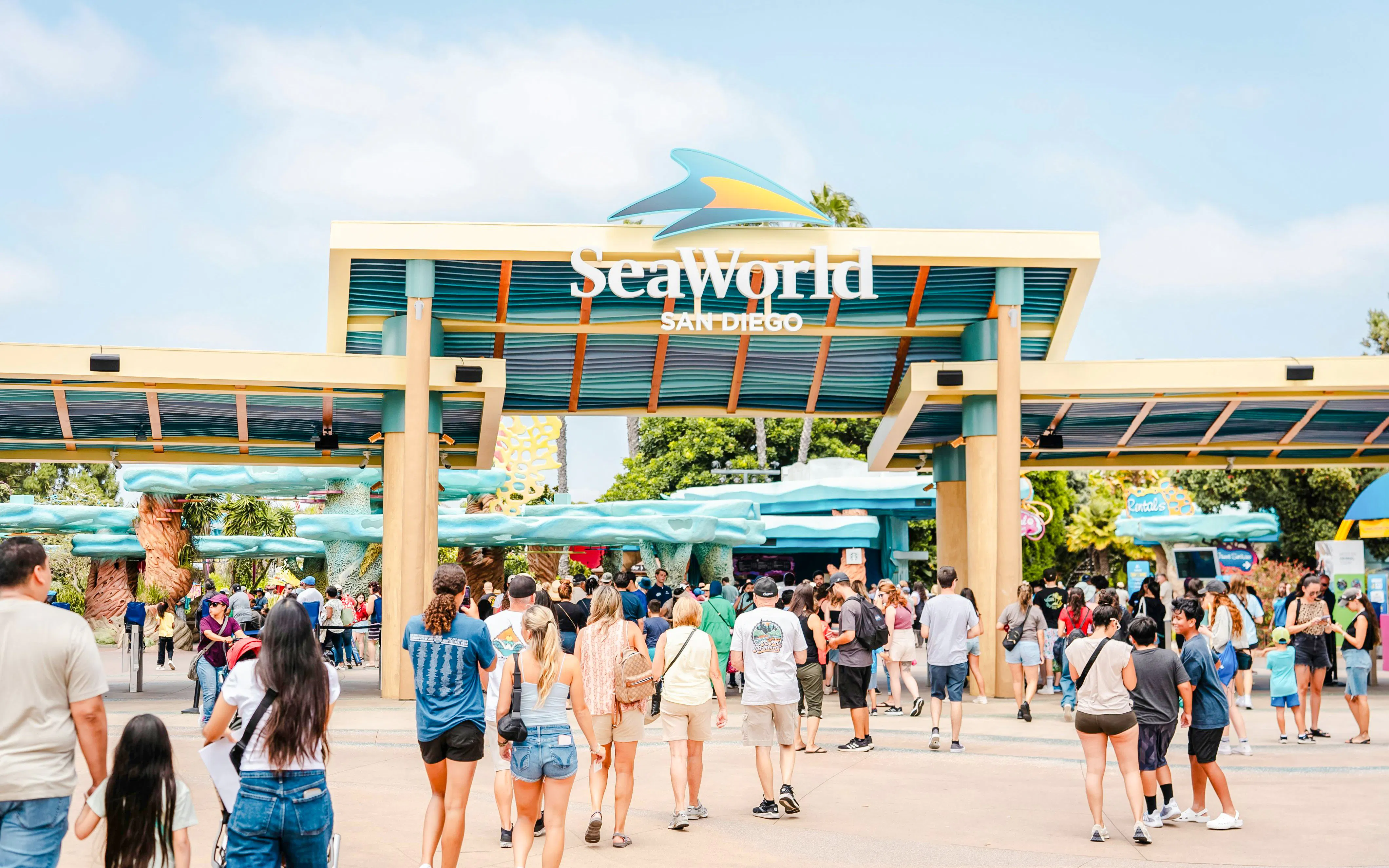 Visitors entering SeaWorld San Diego under the main entrance sign.