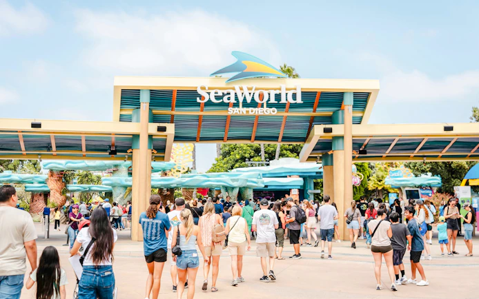 Visitors entering SeaWorld San Diego under the main entrance sign.