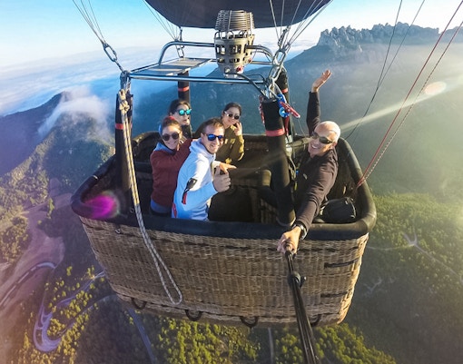 Tourists in a hot air balloon over Montserrat, Spain, with mountain views.