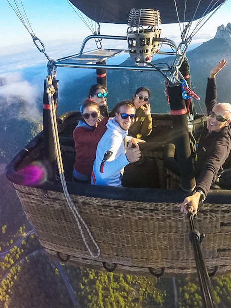 Tourists in a hot air balloon over a scenic landscape with mountains in the background.