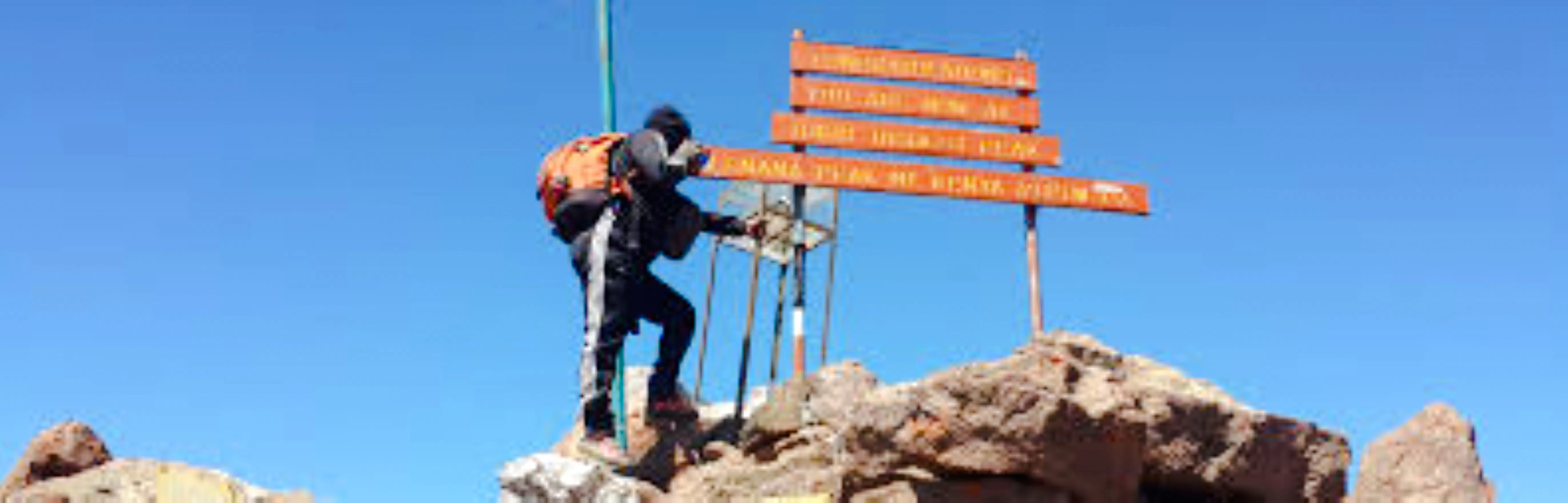 Climber reaching summit sign on Mt Kenya during day tour from Nairobi.