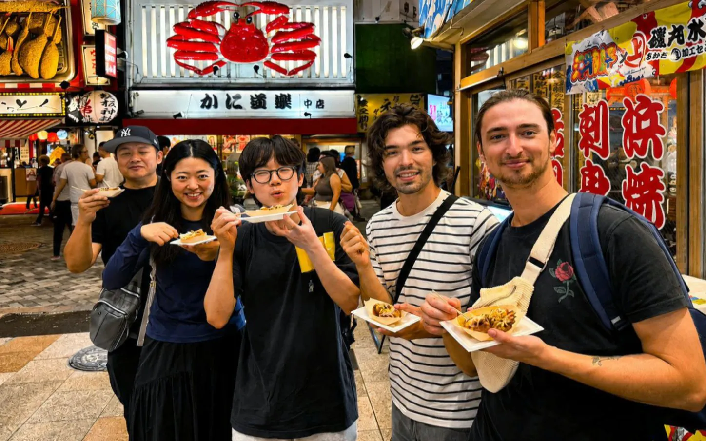 Group enjoying takoyaki on Dotonbori street during a food tour in Osaka, Japan.