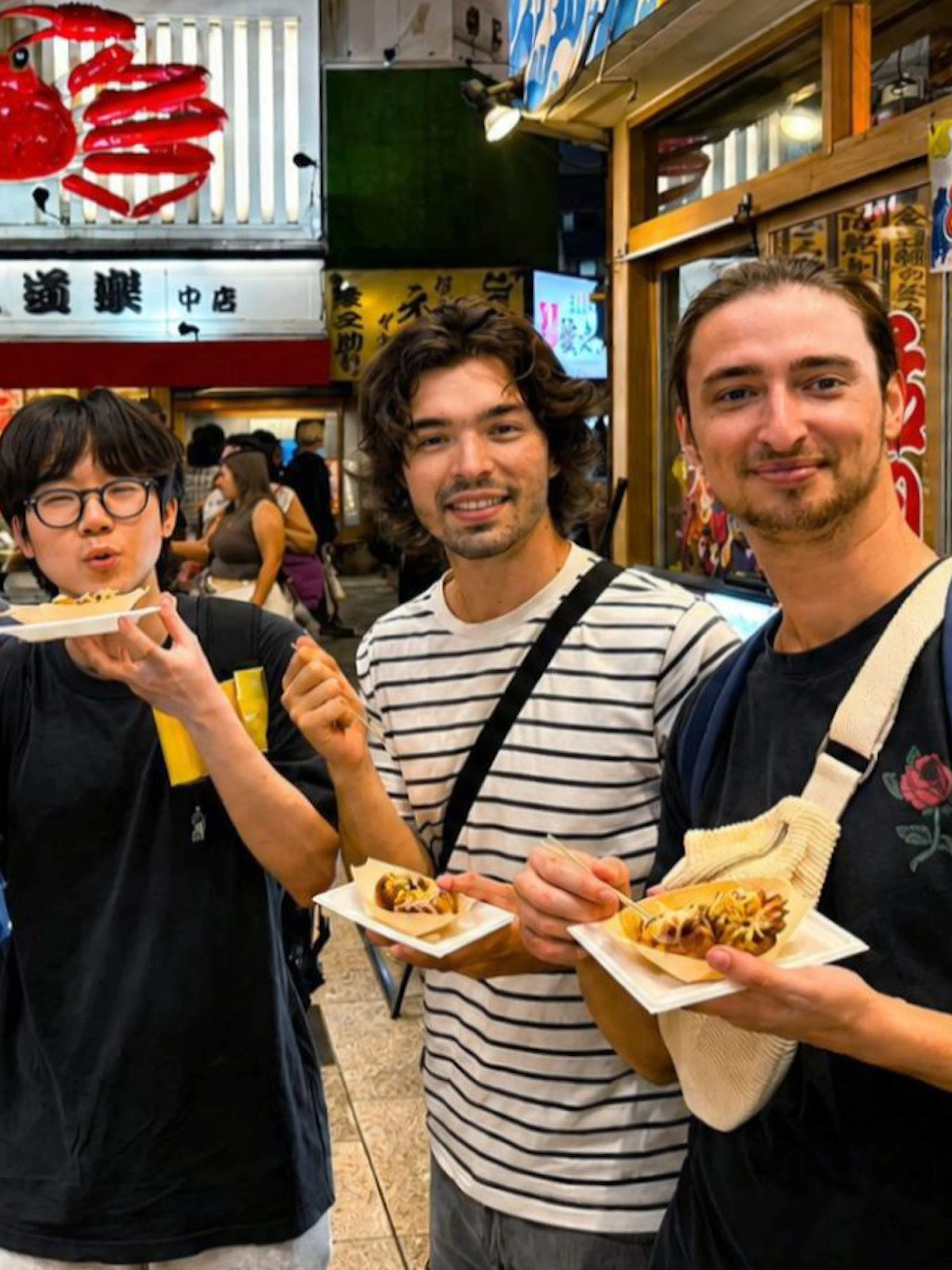 Group enjoying takoyaki on Dotonbori street during a food tour in Osaka, Japan.