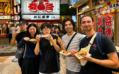Group enjoying takoyaki on Dotonbori street during a food tour in Osaka, Japan.