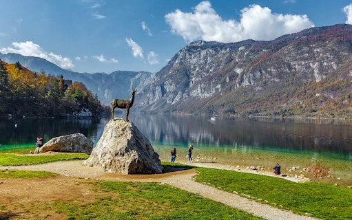 Guests by Bohinj Lake with a goat statue and mountain backdrop in Slovenia.