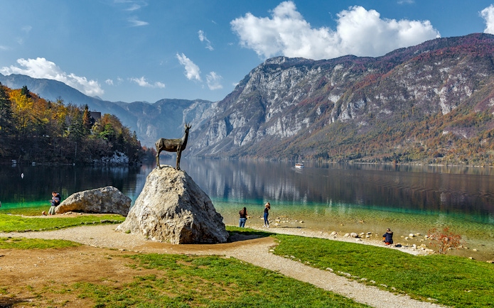 Guests by Bohinj Lake with a goat statue and mountain backdrop in Slovenia.