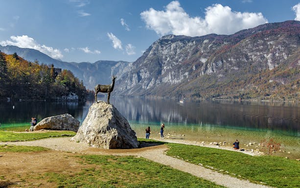 Guests by Bohinj Lake with a goat statue and mountain backdrop in Slovenia.