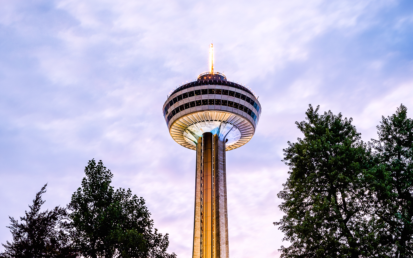 Skylon Tower in Niagara Falls, Canada, viewed from below with surrounding trees.