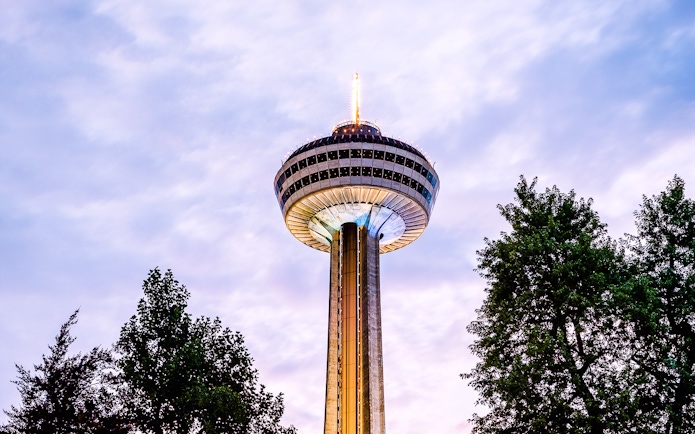 Skylon Tower in Niagara Falls, Canada, viewed from below with surrounding trees.
