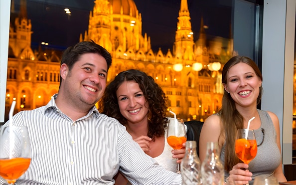 Guests enjoying drinks on a Danube cocktail cruise with Budapest Parliament view.