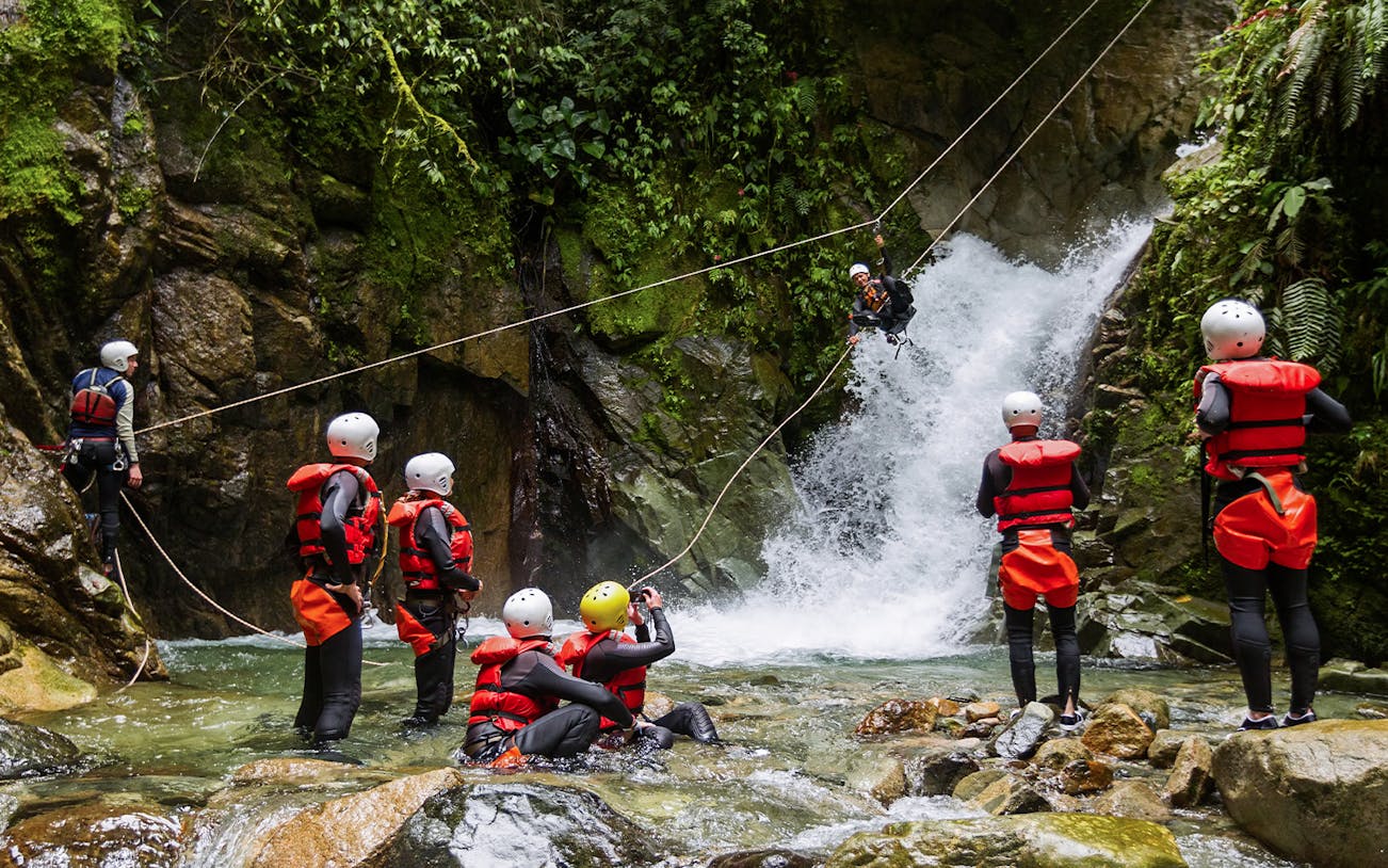 Adventurers ziplining over a waterfall during a water canyoning tour.