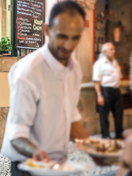 Tourists exploring Alfama's narrow streets with local dining options.