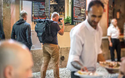 Tourists exploring Alfama's narrow streets with local dining options.