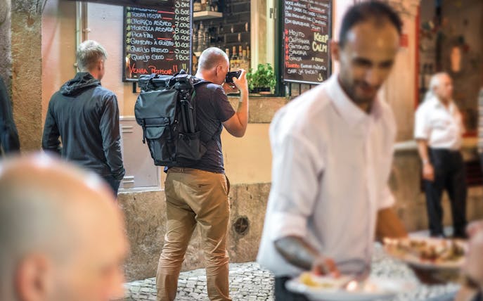 Tourists exploring Alfama's narrow streets with local dining options.