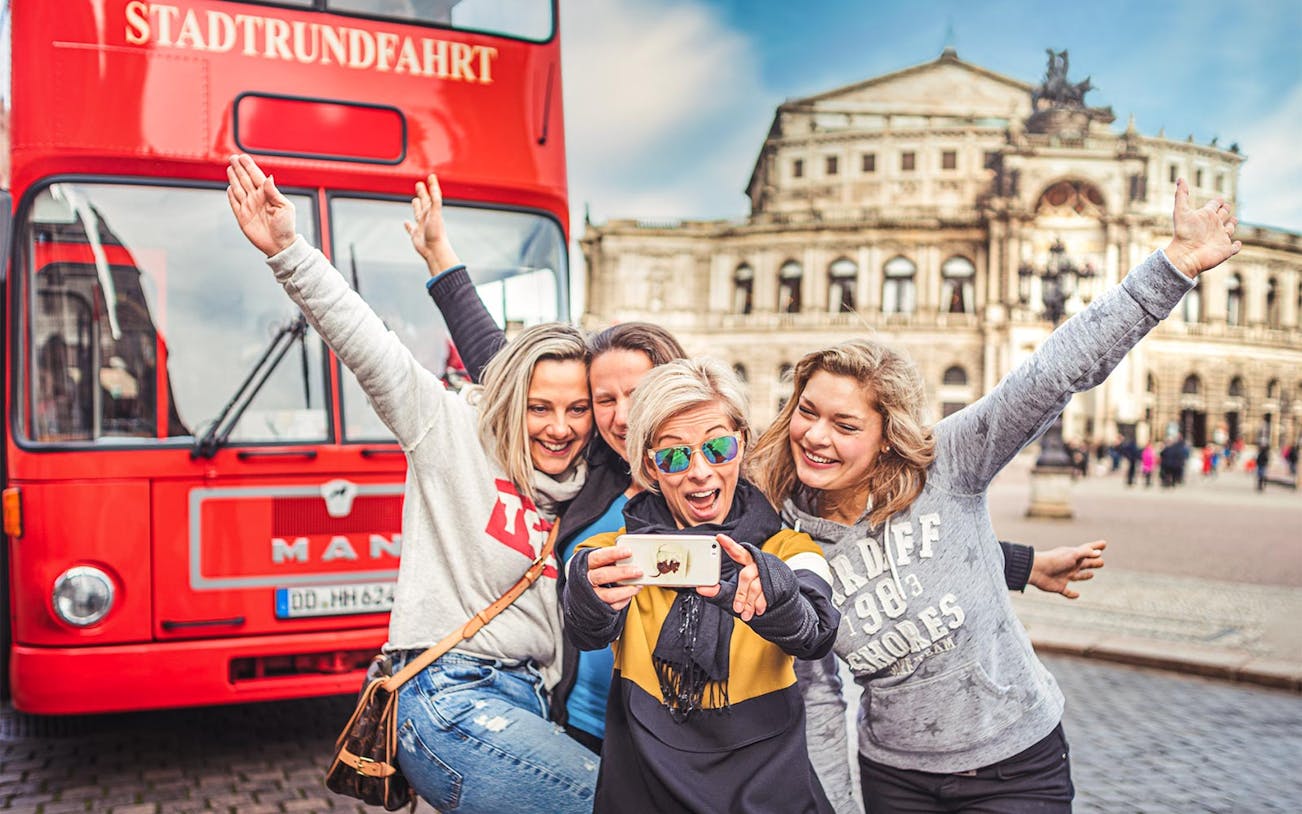 Group taking selfie in front of red tour bus and Semper Opera House, Dresden.