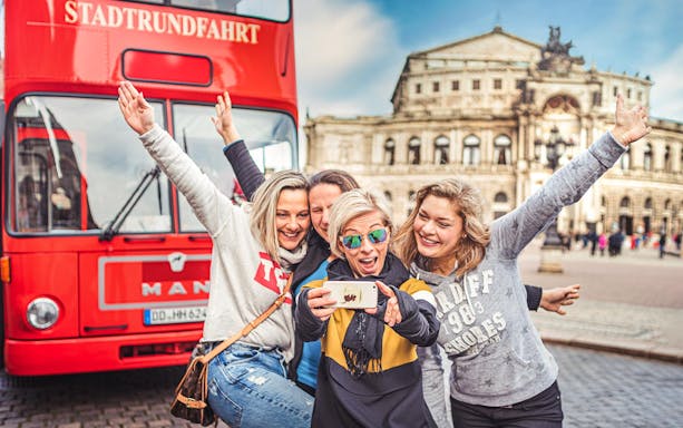 Group taking selfie in front of red double-decker bus in Dresden, Germany.