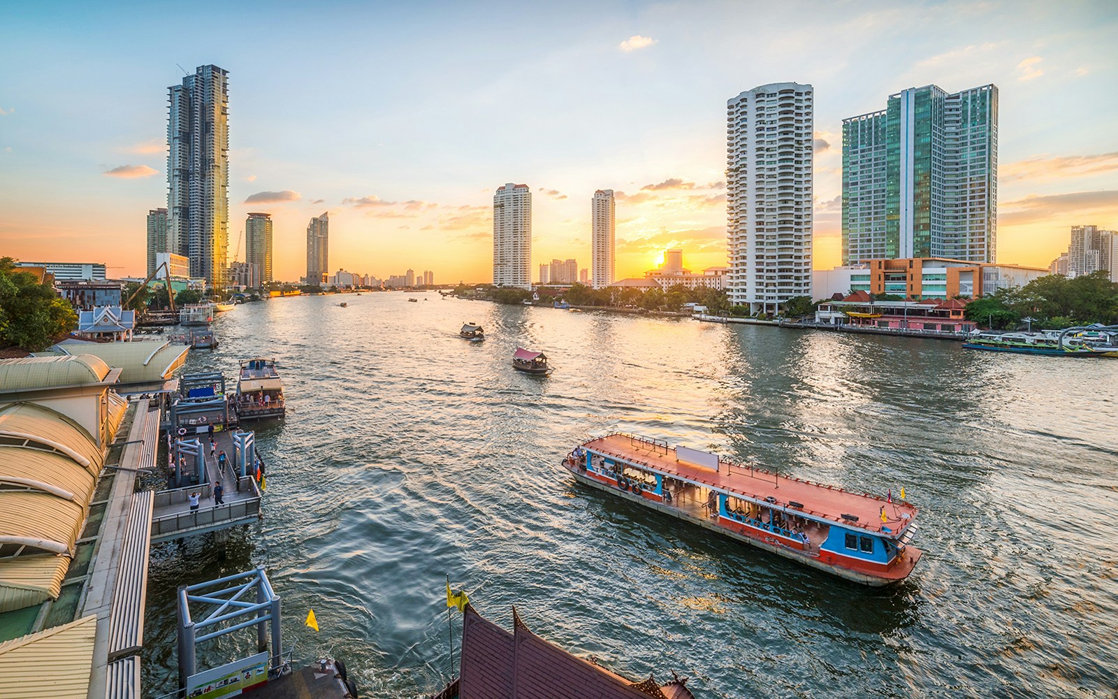 Chao Phraya River with Skyscrapers and Sathon Pier with Boats at Sunset