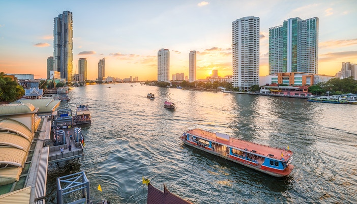 Chao Phraya River with Skyscrapers and Sathon Pier with Boats at Sunset