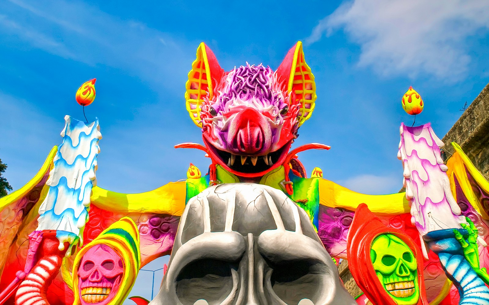 Colorful Halloween carnival float with a large bat and skulls against a blue sky.