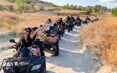 Group enjoying ATV tour on a dirt path in Cappadocia with rocky landscape in the background.