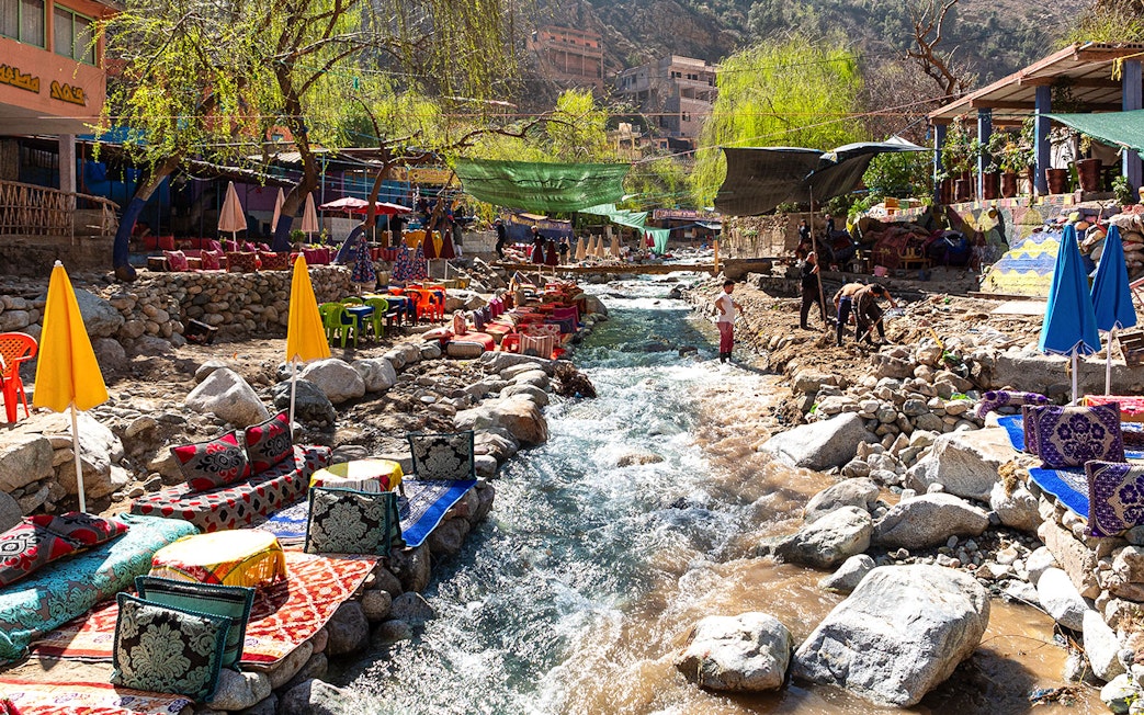 Waterside dining with colorful seating along a stream in Ourika Valley, Morocco.