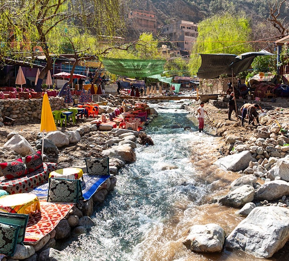Waterside dining with colorful seating along a stream in Ourika Valley, Morocco.