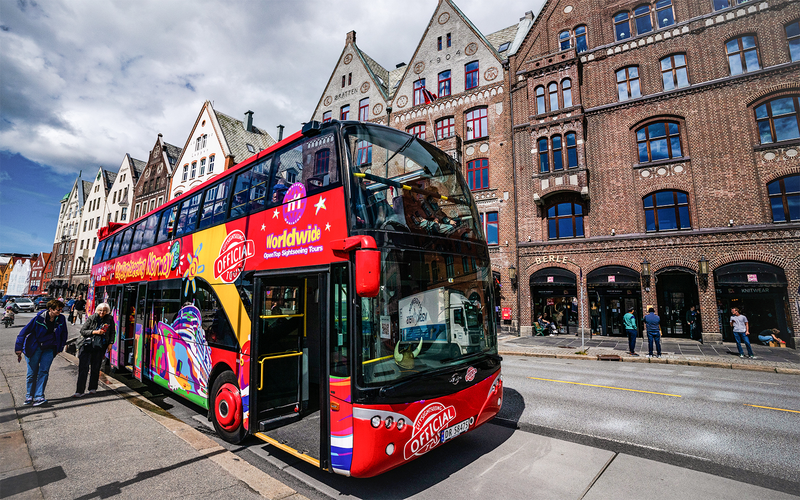 Bergen hop-on hop-off bus in front of historic Bryggen buildings.