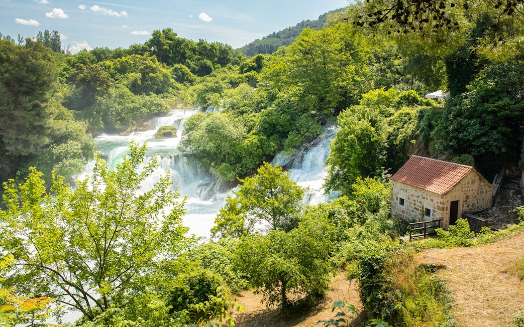 Krka Waterfalls with lush greenery and a stone house, part of a day trip from Split.