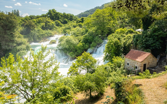 Krka Waterfalls with lush greenery and a stone house, part of a day trip from Split.